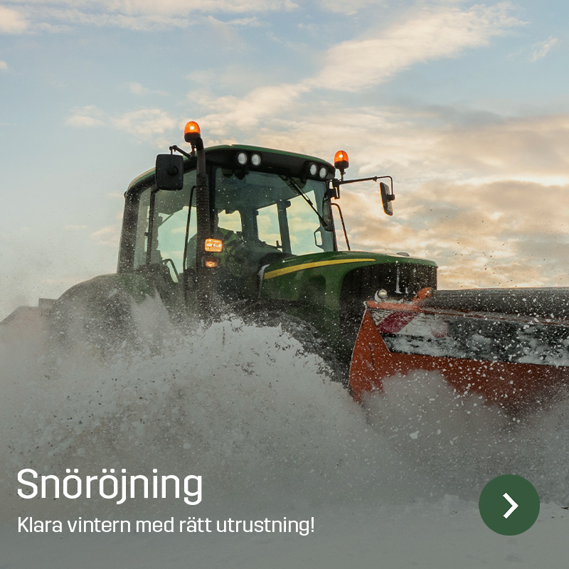En traktor med monterat snöblad röjer kraftig snö och kastar upp snömassor framtill. Bilden visar Sagros utrustning för snöröjning som används för att hålla gårdsplaner och vägar framkomliga under vinterarbete.